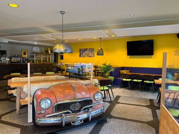 Ansicht TryOut Bar mit Autodekoration und Steinboden und TV. Im Hintergrund sieht man die Bar.
