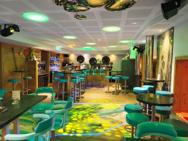 Im Vordergrund hat es einige gemuetliche Sitzgelegenheiten. Blick Richtung Tanzflaeche und im Hintergrund die Bar mit Guckloechern nach aussen. Gemuetliche Lichtstimmung.